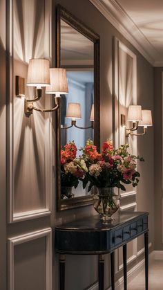 a vase with flowers sitting on a table in front of a mirror and two lamps