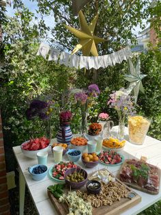 a table filled with lots of food on top of a wooden cutting board next to trees