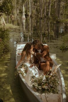 two people are sitting in a boat on the water with flowers and foliage around them