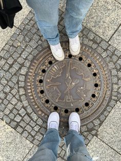 two people standing in front of a manhole cover on the sidewalk with their feet up