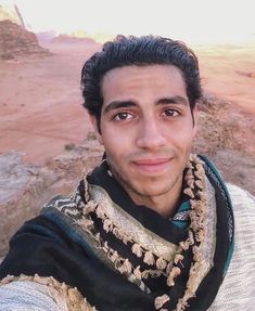 a man with a scarf around his neck posing for a photo in front of the desert