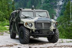 an army vehicle is parked on the side of a road near some trees and mountains