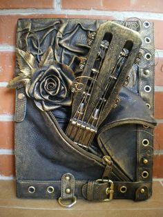 an art piece made out of leather and metal with flowers on the front, sitting against a brick wall