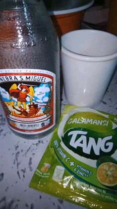 a bag of tangerines next to a bottle of water and a cup on a table