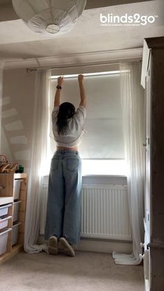 a woman standing in front of a window with her hands up to the light fixture