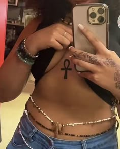 a woman is holding her phone up to show off her stomach and an egyptian symbol tattoo