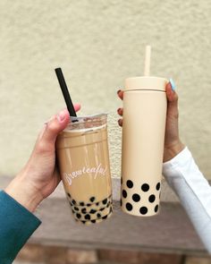 two people holding up coffee cups with straws in each cup and one has a black polka dot design on it