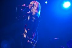 a woman singing into a microphone while standing in front of a stage with blue lights