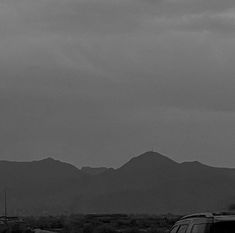 a black and white photo of mountains in the distance with cars parked on the road