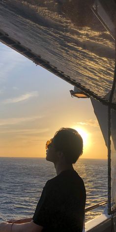 a man sitting on the deck of a boat watching the sun go down over the ocean