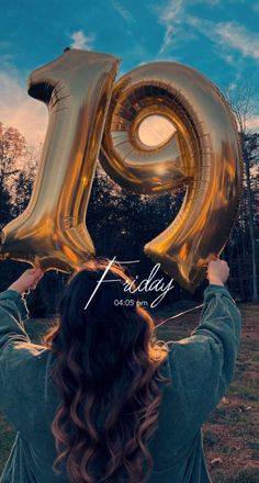 a woman holding up the letter q in front of her face with gold balloons floating over her head