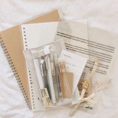 an open notebook, pen, and other items are on a white sheeted surface