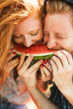 a man and woman kissing while holding a slice of watermelon in front of their face