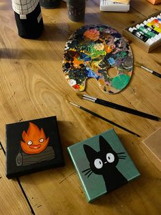 three square paintings on a wooden table with paintbrushes and other art supplies next to them