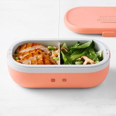 an orange and white lunch box with meat, vegetables and salad in it on a marble surface