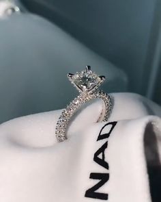 a diamond engagement ring sitting on top of a white cloth with the name nad written on it