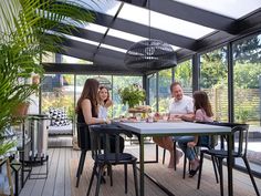 a family sitting at a table outside in the sun on a deck with glass walls