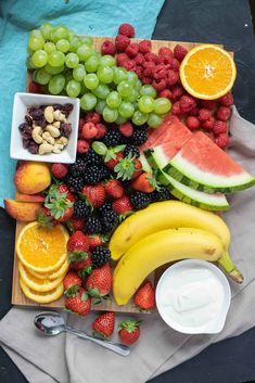 various fruits and vegetables are arranged on a cutting board, including bananas, watermelon, strawberries, grapes, pineapples, almonds