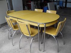 a yellow table and four chairs in a room with concrete flooring on the ground