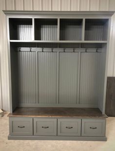 a large gray bookcase with drawers and two coats on it's sides, in front of a white wall