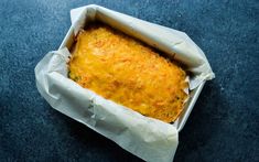 a casserole in a paper container on a blue surface with white wax paper