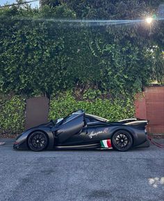 a black race car parked in front of a hedge