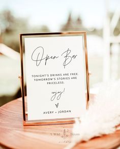 an open box sign sitting on top of a wooden table next to a white feather