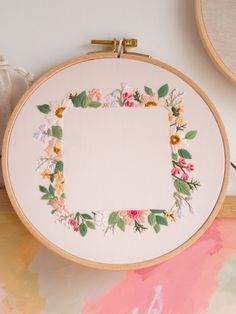 an embroidered frame with flowers on it next to some scissors and other crafting supplies