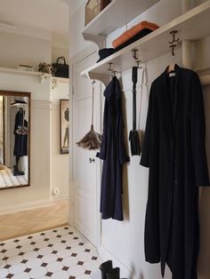 two coats hanging on hooks next to a mirror and coat rack in a room with tiled flooring