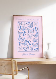 a pink poster with blue butterflies on it next to a white vase and gold chair