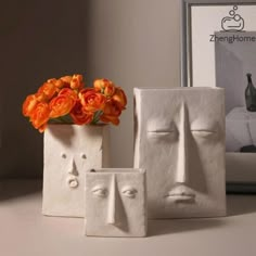 two white vases with orange flowers in them sitting on a table next to a framed photograph