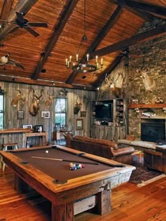 a pool table in the middle of a living room with wood floors and exposed ceiling