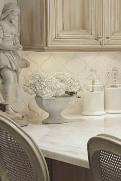 a white kitchen with marble counter tops and wooden cabinetry, along with vases filled with flowers