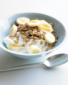 a bowl filled with yogurt, granola and sliced banana's next to a spoon