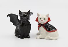 two black and white cats sitting next to each other on a white surface with one cat wearing a red bow