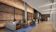 two people sitting on couches in an office lobby with exposed brick walls and floor to ceiling windows