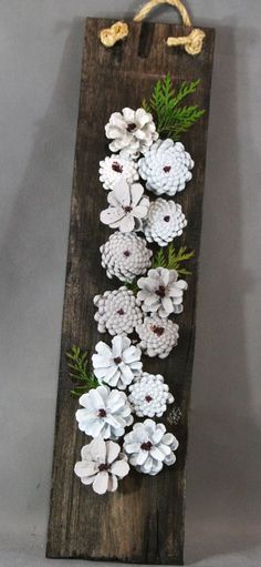 a wooden sign with pine cones and white flowers on it, hanging from a rope