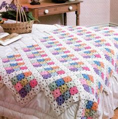 a crocheted granny blanket on top of a bed next to a wooden table