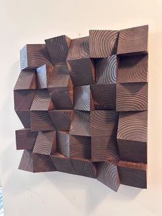 a wooden wall sculpture made out of wood planks on a white wall next to a blue vase