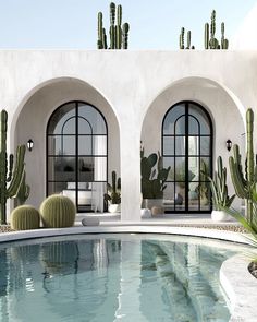 an outdoor swimming pool surrounded by cactus and potted cacti in front of two arched windows