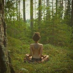 a woman sitting in the middle of a forest doing yoga