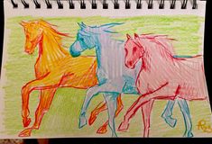 a drawing of three horses in different colors on a sheet of paper with colored crayons