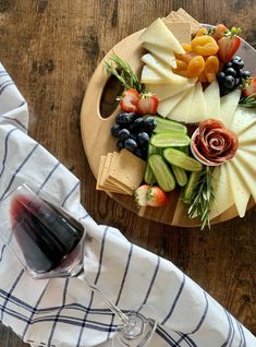 a wooden platter filled with fruit and cheese next to a glass of red wine