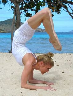 a woman doing a handstand on the beach in front of some water and trees