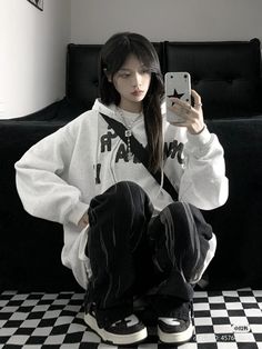 a young woman sitting on top of a black and white checkered floor holding a cell phone