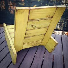 a yellow wooden bench sitting on top of a wooden deck next to a fence and bushes