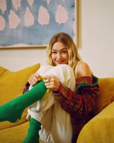 a woman sitting on top of a yellow couch next to a green leg high socks