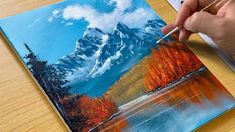 a person is painting a mountain scene with acrylic paint on a piece of wood