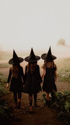 three girls wearing witches hats walking down a dirt road