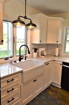 a kitchen with white cabinets and an island in front of two windows that look out onto the yard